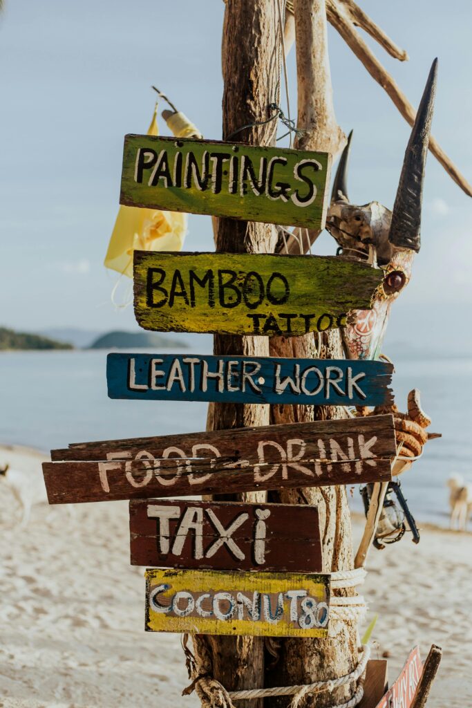 Vibrant wooden signpost on a sandy beach offering various services. Perfect for travel-themed content.